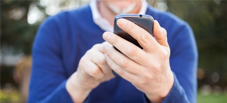 Hombre revisando su teléfono después de recibir una alerta por mensaje de texto de Humana Pharmacy acerca de su próximo pedido